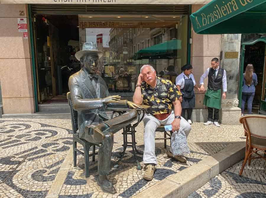 Sitting next to the bronze statue in front of the A Brasileira Café,